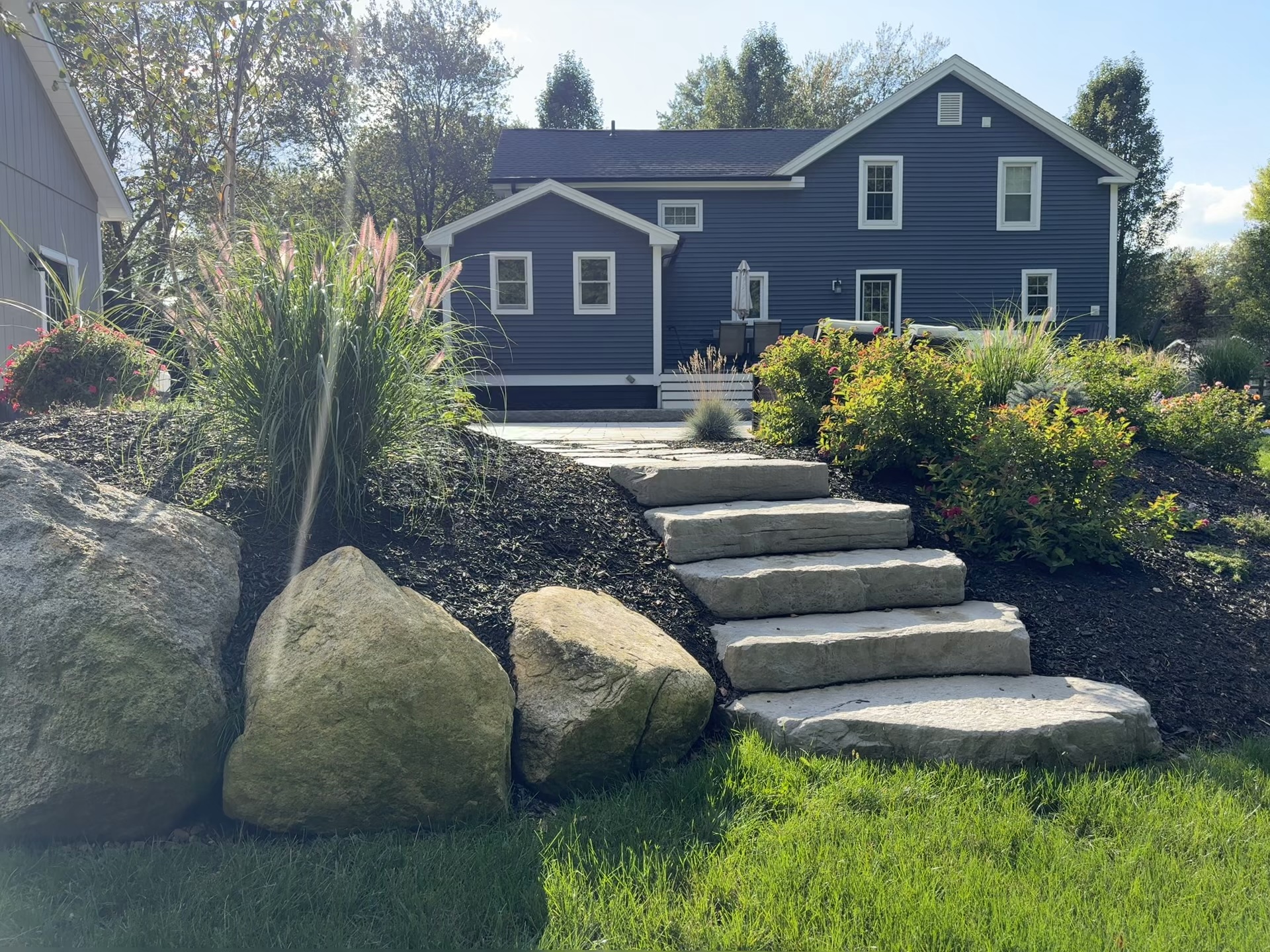 Natural stone stairway with boulder walls and full landscape beds behind a navy farmhouse in Ellington, CT