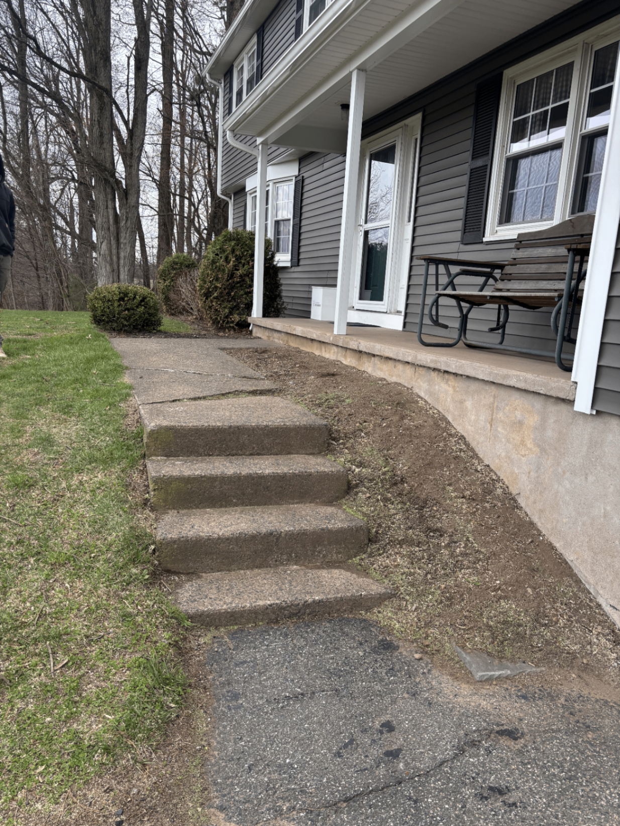 Cracked concrete steps and worn walkway beside a covered porch before replacement