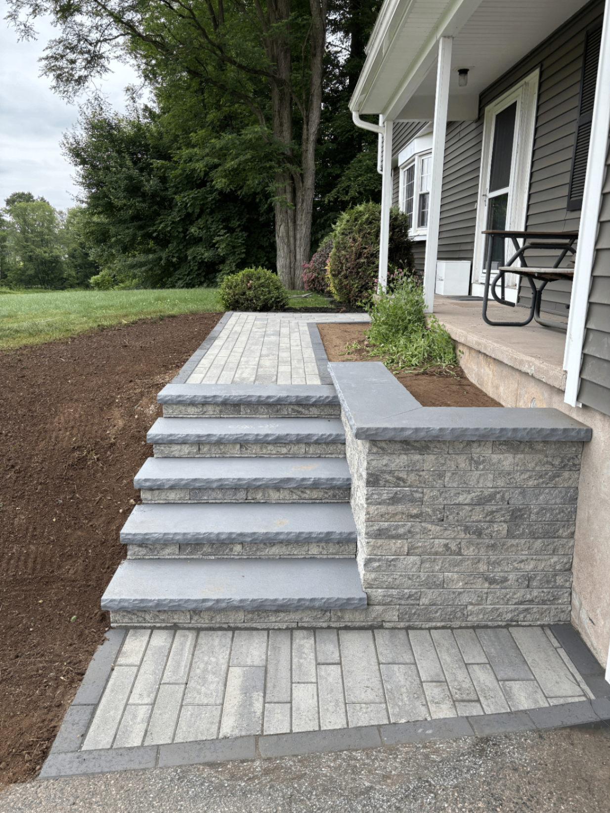 New paver walkway with bluestone-capped steps and a stone retaining wall