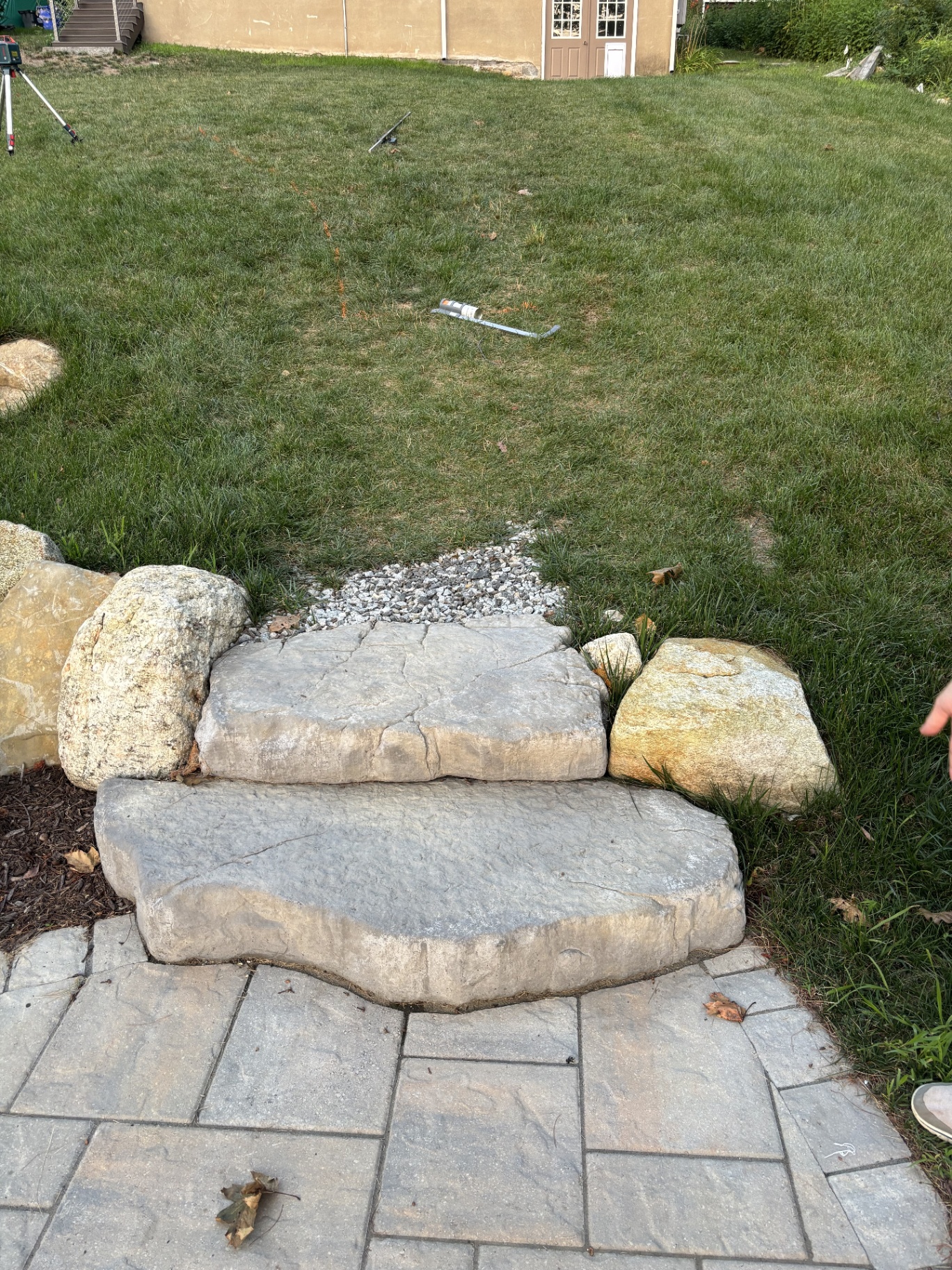 Single stone step and boulder edge at the top of a paver patio before landscaping