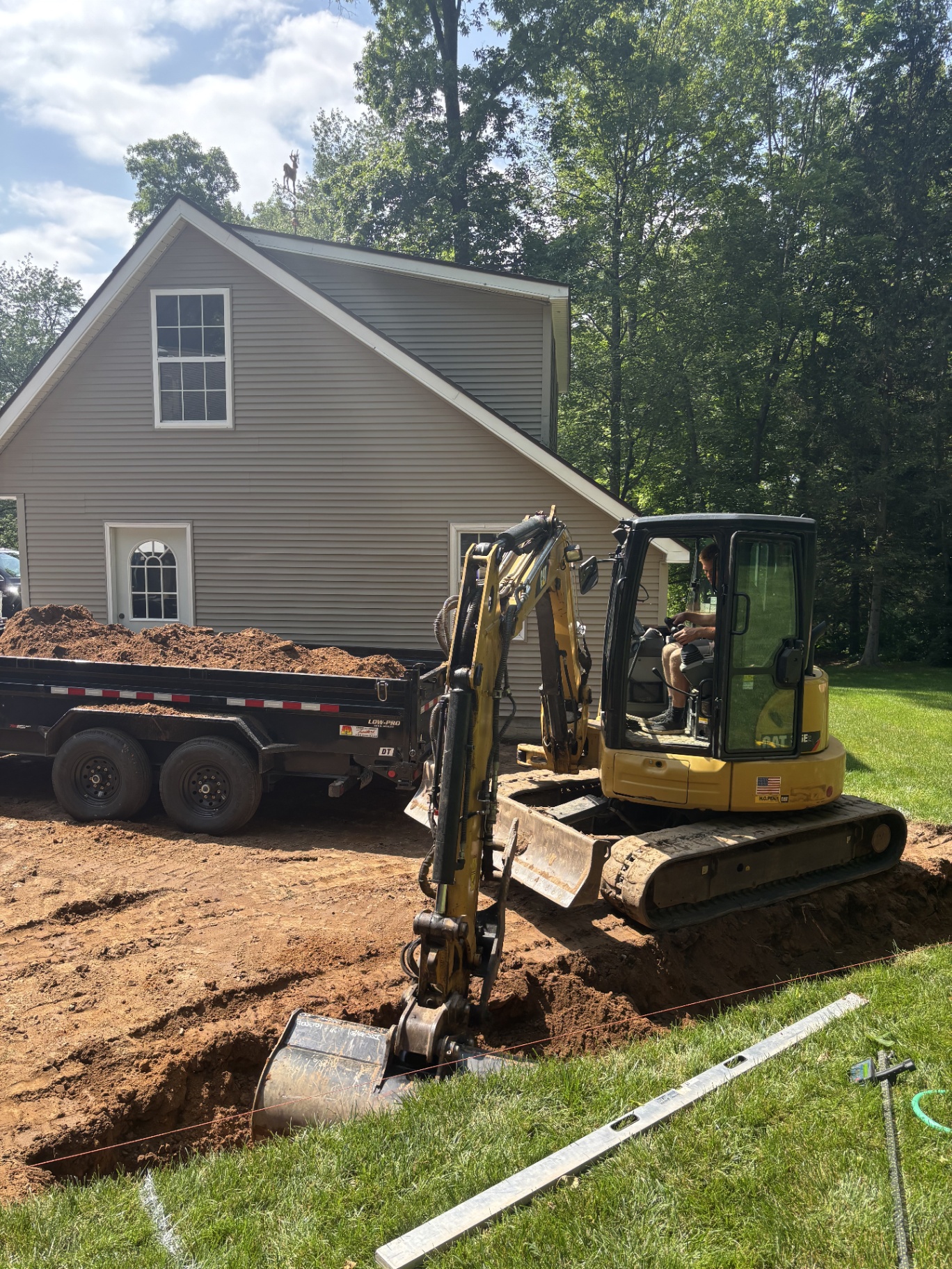 Excavator digging the footing trench for a new retaining wall beside the house
