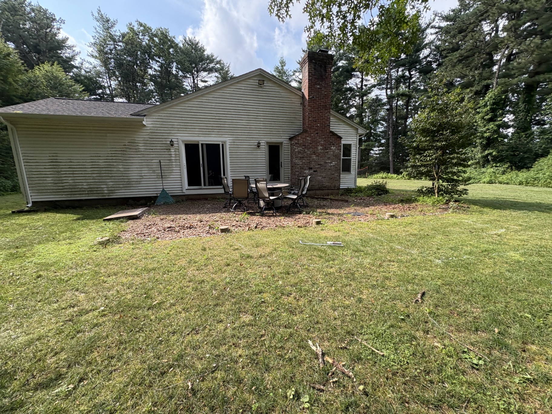 Backyard with worn mulch seating area behind a vinyl-sided home before the patio build