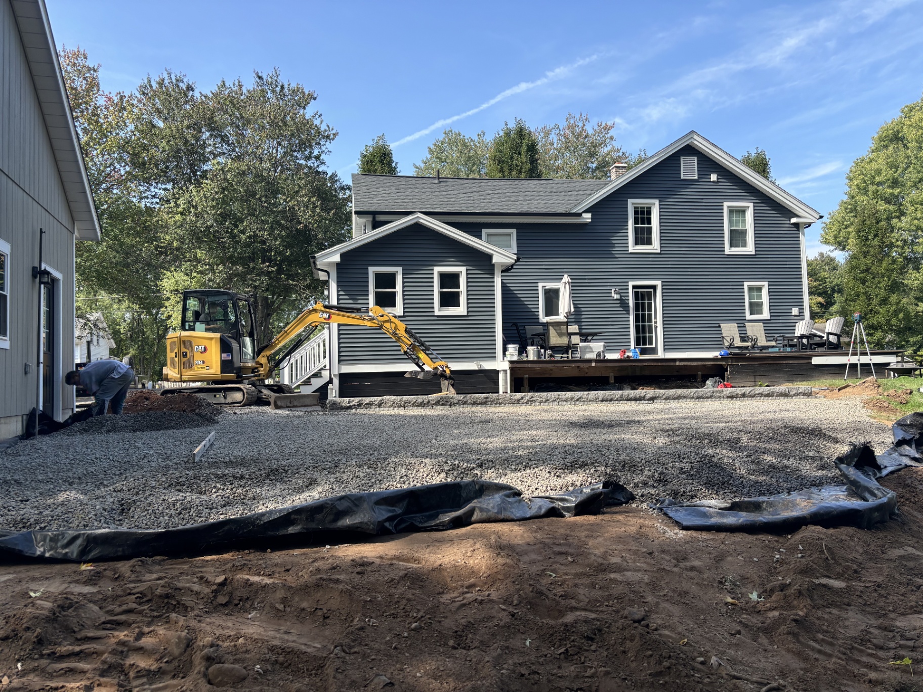 Backyard excavated with gravel base and an excavator before the patio and plantings
